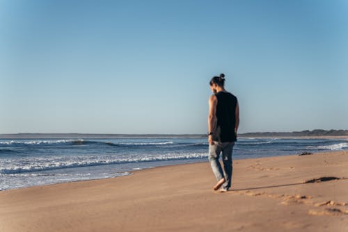 Anonymous man walking on empty sandy seashore