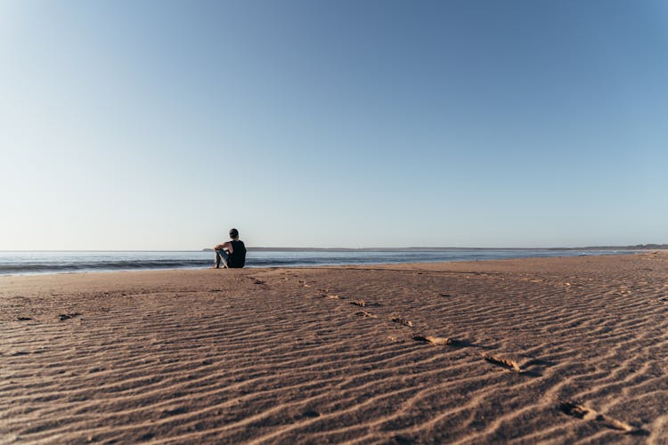 Unrecognizable Man Sitting On Sandy Beach And Enjoying Sea Views