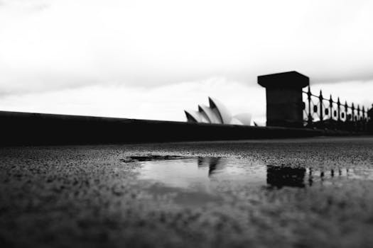 A black and white perspective of Sydney Opera House with a reflective puddle in the foreground.