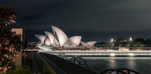 Free Unusual design of white Sydney Opera House with large concrete panels forming shells located on city harbor at night Stock Photo