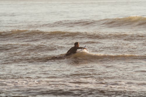 Side view of sporty male with surfboard catching wave in rippling water of ocean