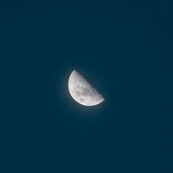 夜晚，半个月亮带着陨石坑的痕迹，在无云的黑暗天空中升起