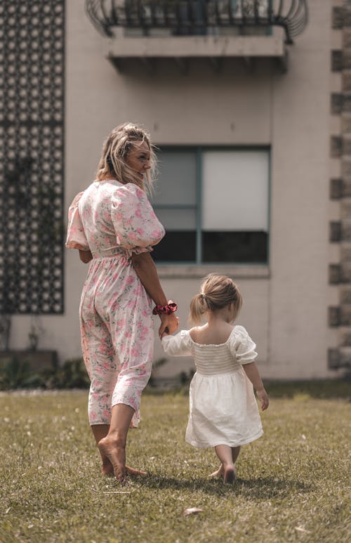 Mother with daughter walking on grass near building