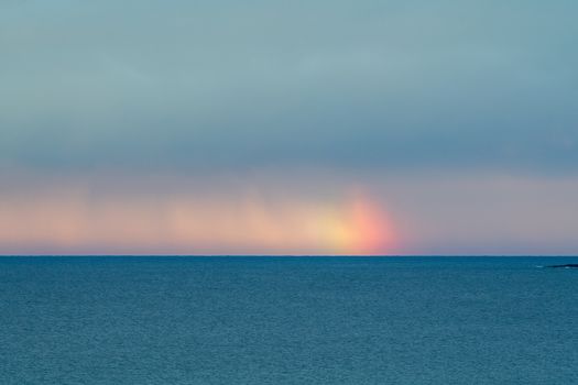 阴云密布的天空下，一道淡淡的彩虹映衬着宁静的海景，让人捕捉到大自然的静谧之美