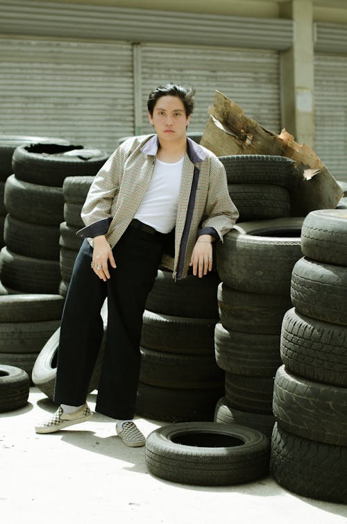 Free Full length of Asian female in jacket leaning on tires and looking at camera in sunlight Stock Photo