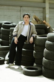 一位穿着夹克的亚洲女性靠在轮胎上，在阳光下看着相机
