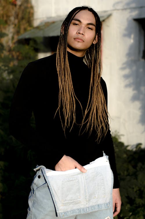 Confident ethnic androgyny with long hair wearing black turtleneck and denim overall looking at camera