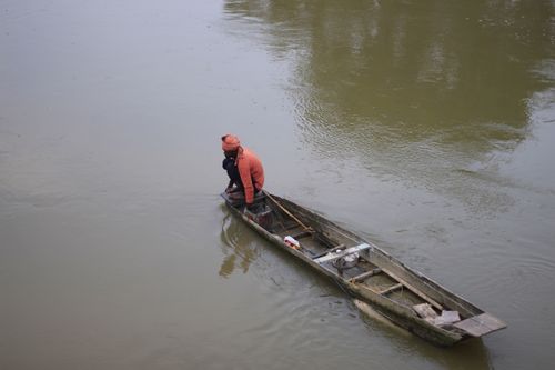 Free A man in a red shirt fishes alone on a river in a wooden boat. Stock Photo