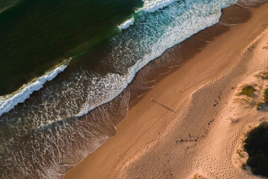 From above of foamy waves of azure sea washing sandy coastline in tropical country on summer day in nature in sunlight