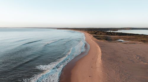 Free Picturesque seascape with foamy waves of sea rolling sandy shore in nature with green bushes in distance against cloudless sky Stock Photo