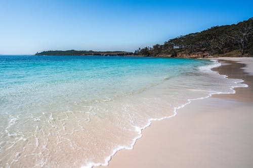 Turquoise sea rolling on sandy beach with green forest in tropical lagoon against blue sky in nature on summer day