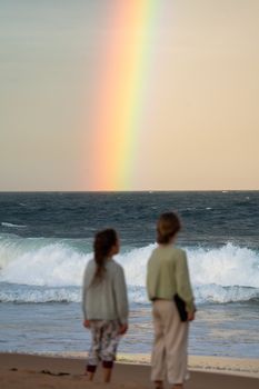 两个孩子在海滩上看着海浪上的彩虹