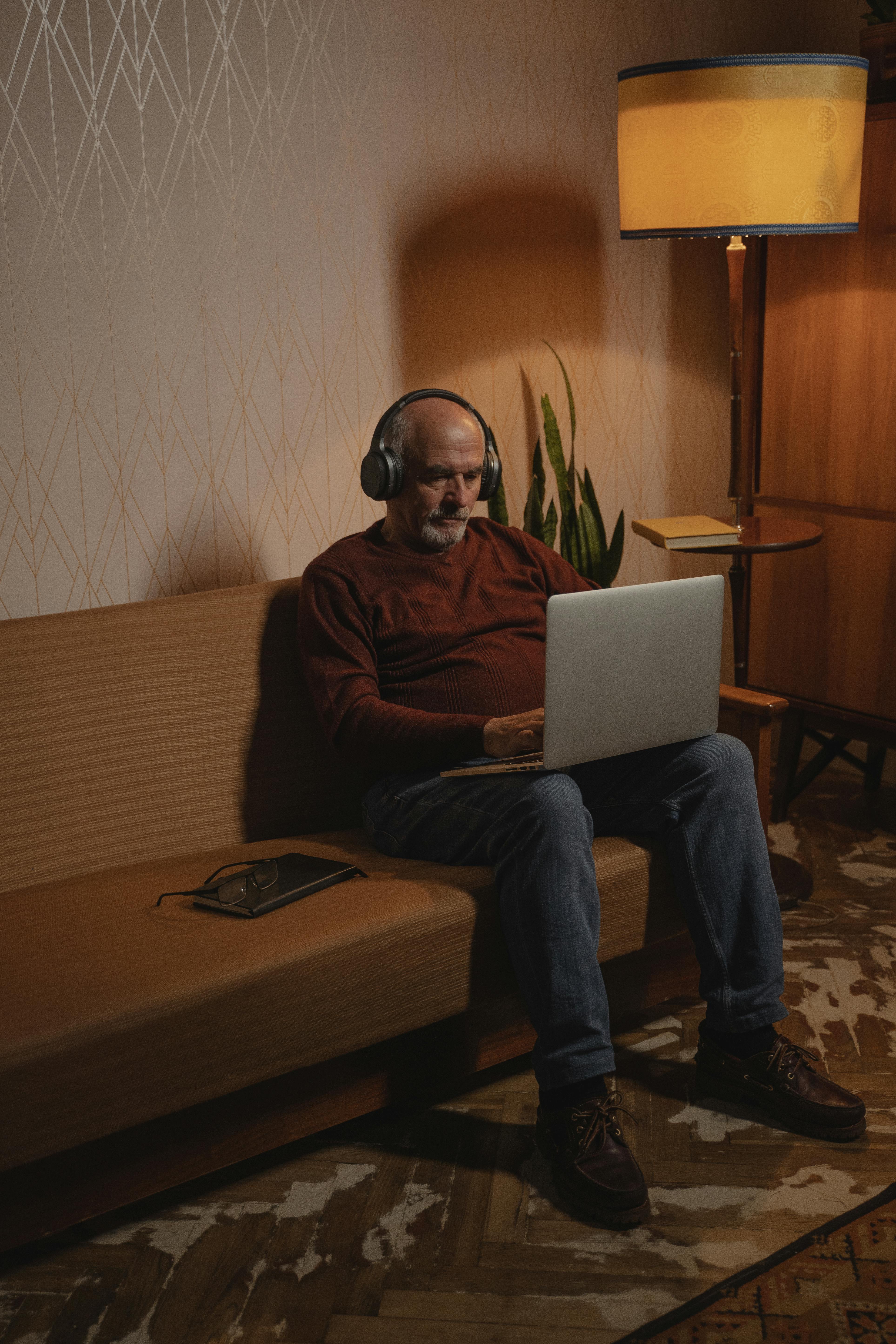 an elderly man sitting on the couch while using his laptop