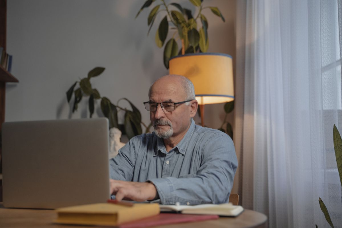 Un hombre mayor escribiendo en su computador portátil en casa