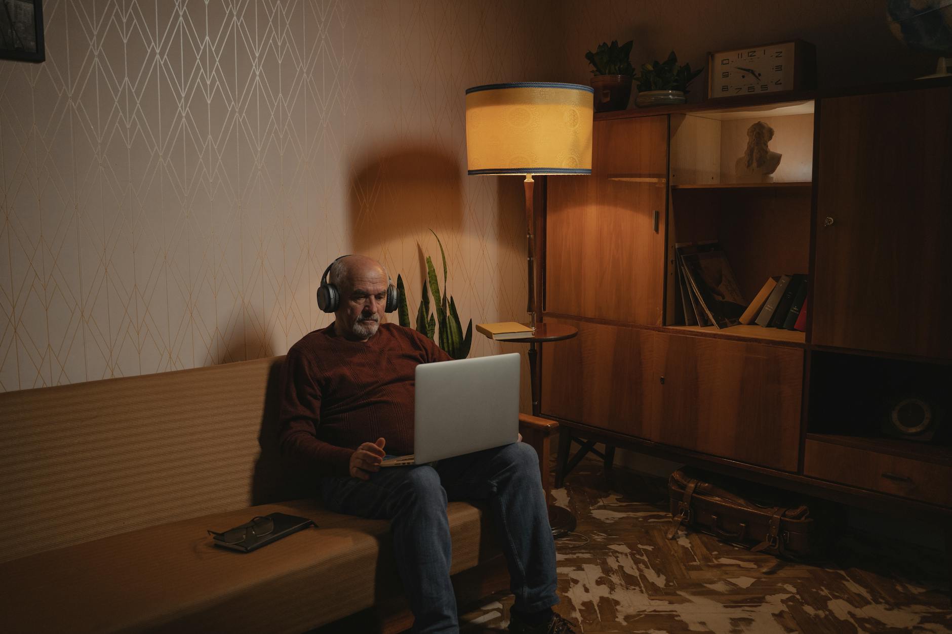 Elderly man video calling on a laptop in a cozy living room with warm lighting.