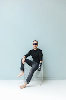 Fashion-forward photo of a man with a prosthetic hand seated barefoot, sporting a futuristic vibe.