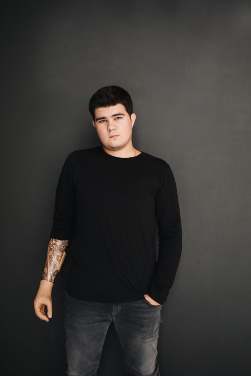 Free Stylish portrait of a man in black attire with tattoo on forearm against a black background. Stock Photo