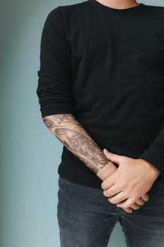 Close-up of a man's tattooed arm and casual attire against a plain background.