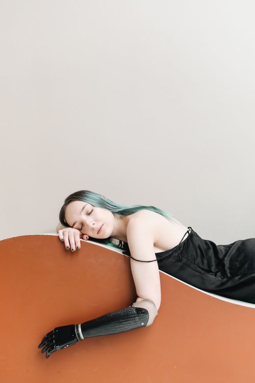 Free Caucasian woman with prosthetic arm rests peacefully. Modern and minimalistic setting, conveying a sense of tranquility. Stock Photo