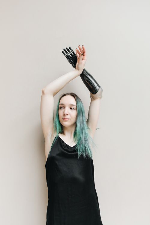 Free Confident woman in a studio showcasing her prosthetic arm, wearing a black dress. Stock Photo