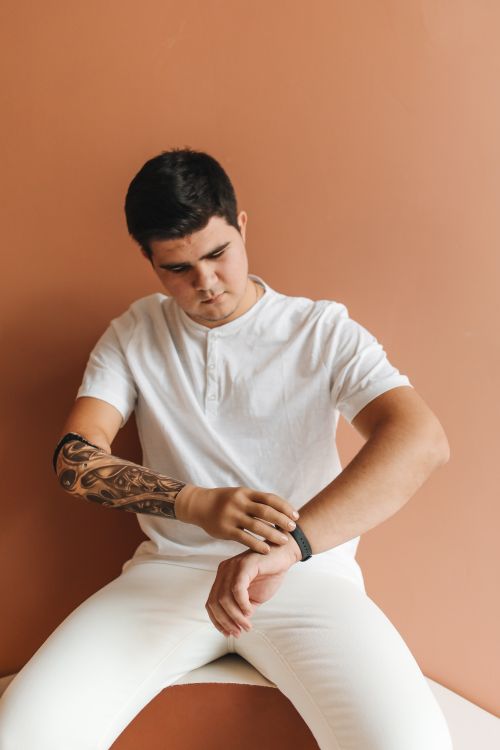 Free Adult man in white attire adjusts wristwatch on prosthetic arm against brown backdrop. Stock Photo