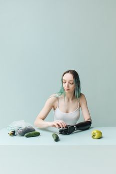 Young woman with a prosthetic hand sits at a table with cucumbers and a yellow pepper.