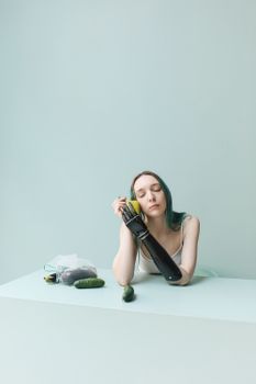 一名年轻女子戴着假肢，坐在柔和的绿色桌子上，手里拿着黄瓜和苹果