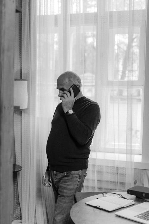 A Man Talking on the Phone Near the Window