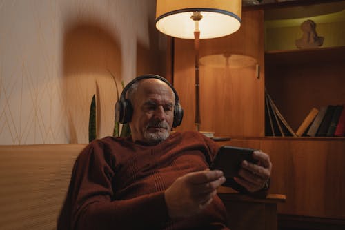 Photograph of an Elderly Man with Headphones Holding His Phone