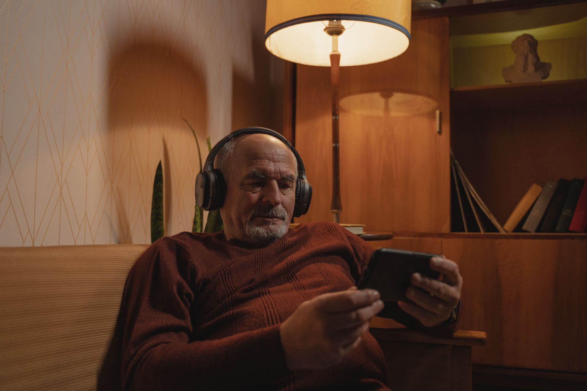 Photograph of an Elderly Man with Headphones Holding His Phone