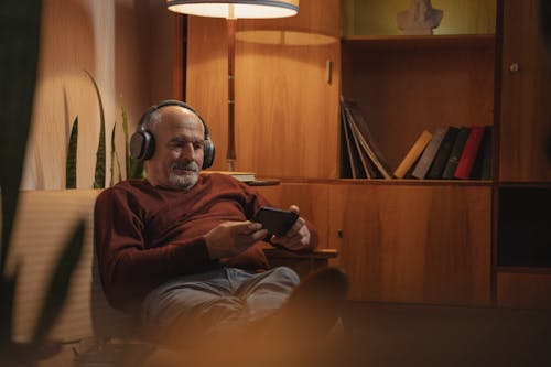 Photo of an Elderly Man Watching on His Phone Near a Lamp