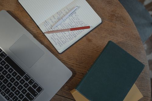 Free A clean, organized workspace featuring a laptop, notebooks, and pens on a wooden table, perfect for productivity. Stock Photo