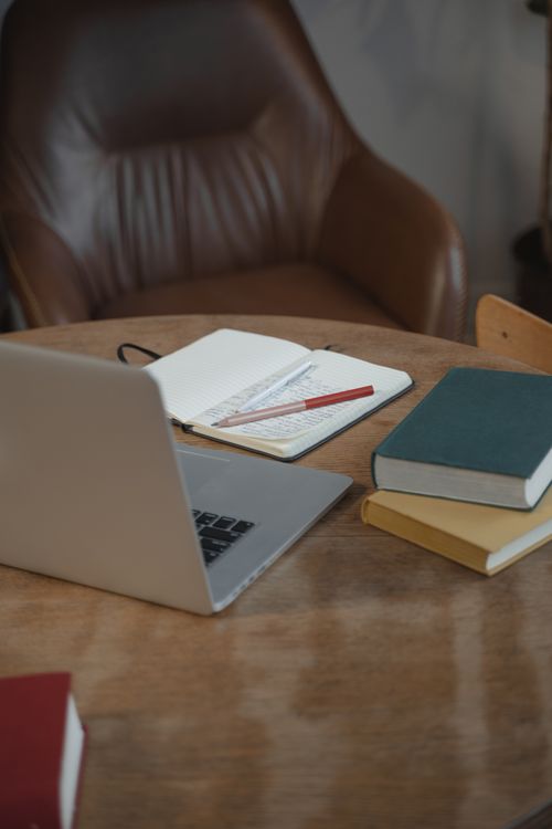 Free A warm indoor workspace featuring a laptop, notebooks, and books on a wooden table. Stock Photo