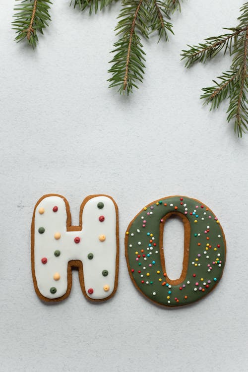 Top view of creative gingerbread letters decorated with glaze and colorful sparkles arranged on white background with fir branch during Xmas holidays