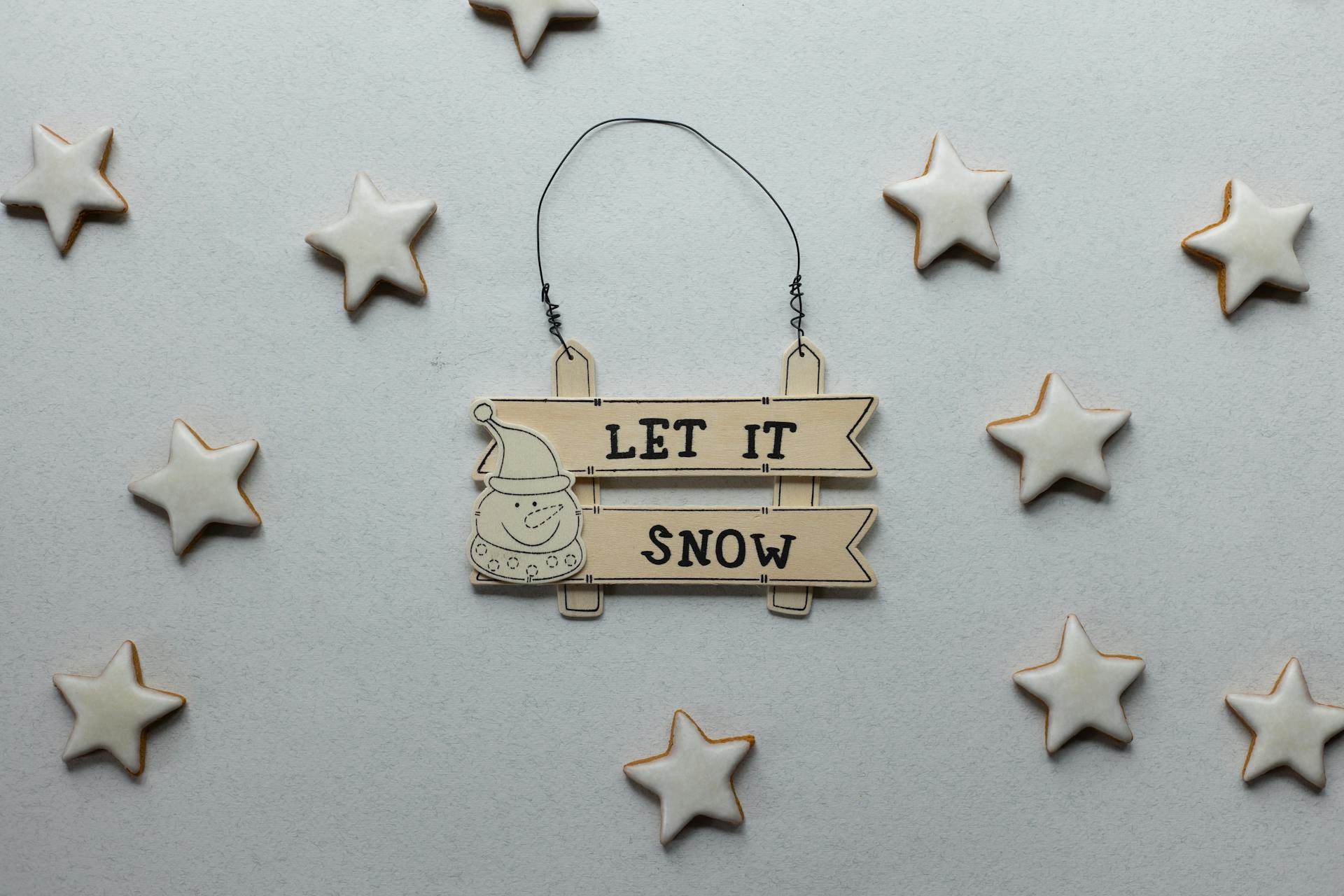 Overhead view of wooden signboard with inscription and snowman surrounded by delicious gingerbread stars during New Year holiday on gray background