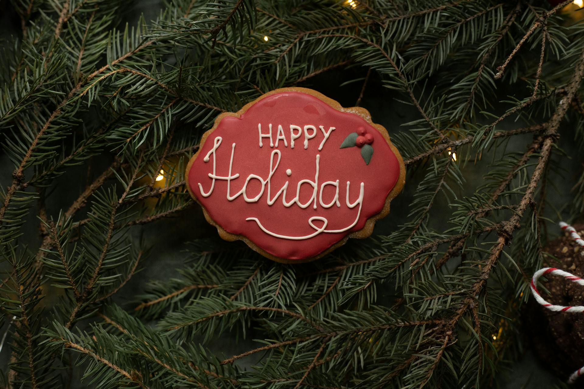 Top view of delicious gingerbread biscuit with bright icing and inscription on coniferous tree sprigs during New Year holiday