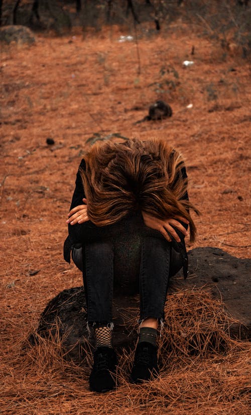 A Sad Woman Sitting on a Rock Near Hay