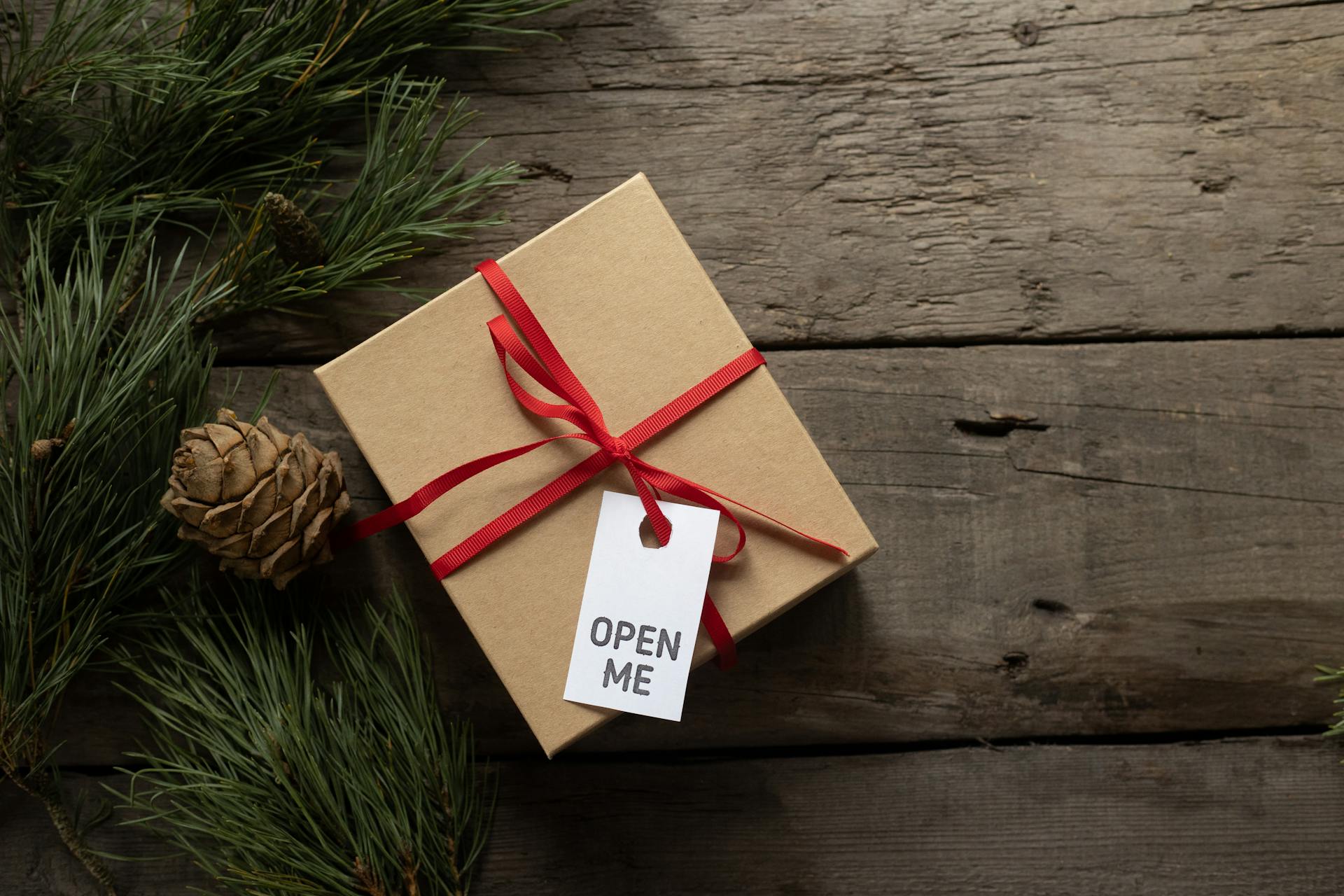 Eco-friendly Christmas gift wrapped in recycled paper with a red ribbon and "Open Me" tag on a wooden surface.