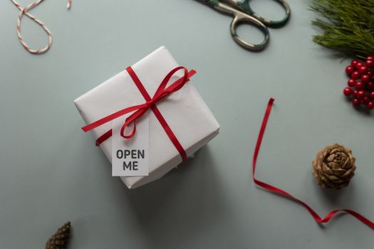 Top view of present box with Open Me inscription on tag and ribbon bow near pine cones on light background