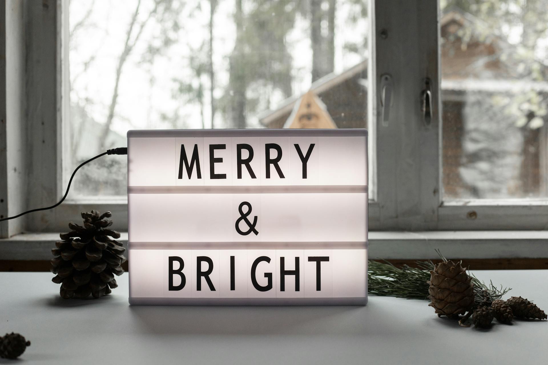 Lightbox with 'Merry & Bright' message on a windowsill, surrounded by festive decor.