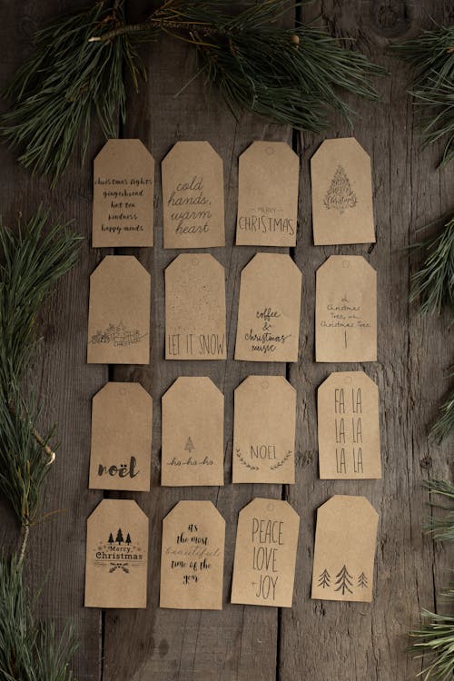 Collection of small paper Christmas tags arranged on wooden table and surrounded by pine branches on festive season