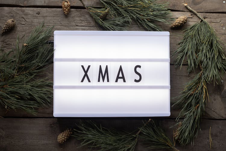 Lamp With Word Xmas On Table Near Pine Branches