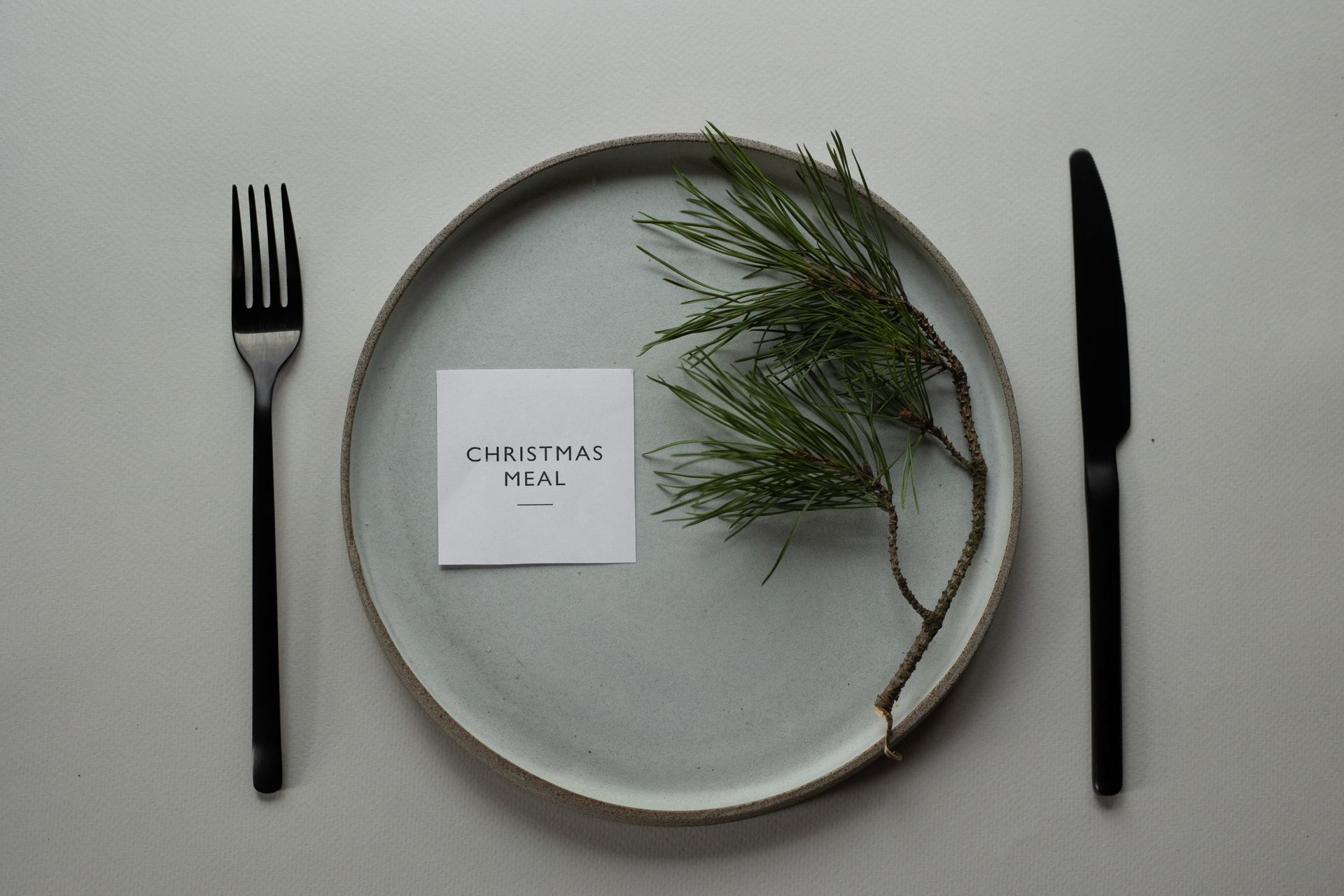 Elegant Christmas meal table setting with pine twig and card, perfect for holiday celebrations.