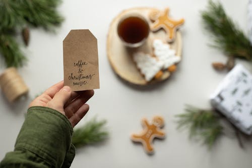 Selective focus of male hand holding brown paper tag with sign Coffee And Christmas Music and Christmas composition on background