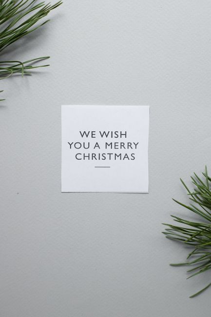 We Wish You A Merry Christmas on white paper sheet placed on surface with green coniferous branches on gray background