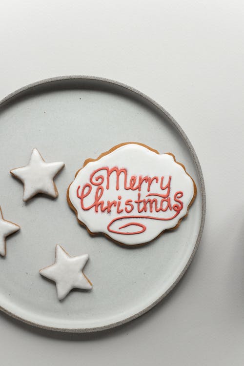 From above composition of gingerbread cookie with Merry Christmas wish inscription and small star shaped cookies placed on white ceramic plate