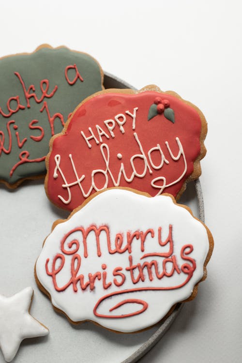 From above of tasty baked cookies made for Christmas celebration covered with colorful icing and inscriptions placed on ceramic plate