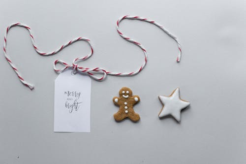 Free Overhead composition of handmade gingerbread man and star cookies covered with icing placed near gift tag with string and inscription Merry And Bright Stock Photo