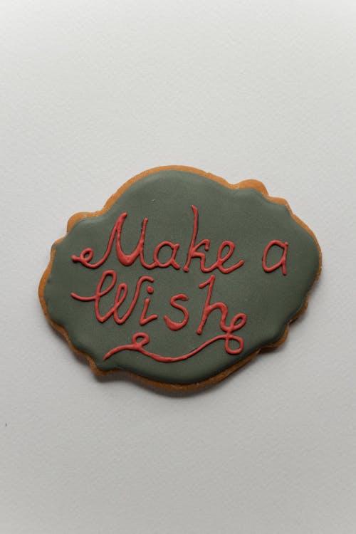 Top view of Make A Wish lettering on green icing of gingerbread baked cookie placed on gray background during Christmas holiday