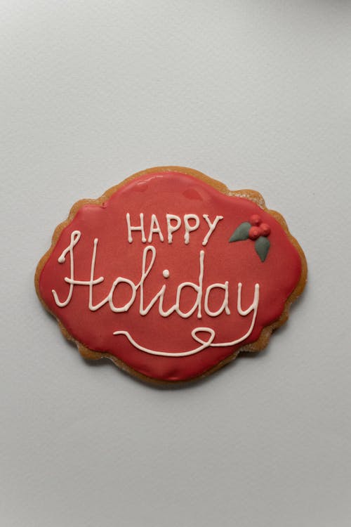 Top view of white Happy Holiday inscription on red icing of gingerbread cookie placed on gray background during Christmas celebration
